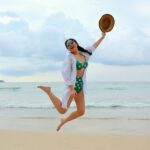 Woman Jumping on Seashore and Holding Hat