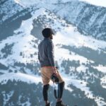 Man Wearing Gray Long-sleeved Shirt and Brown Shorts Holding Black Dslr Camera on Mountain