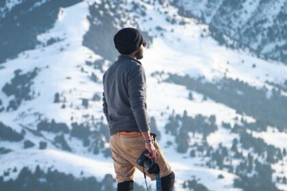 Man Wearing Gray Long-sleeved Shirt and Brown Shorts Holding Black Dslr Camera on Mountain