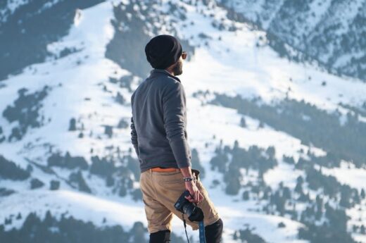 Man Wearing Gray Long-sleeved Shirt and Brown Shorts Holding Black Dslr Camera on Mountain