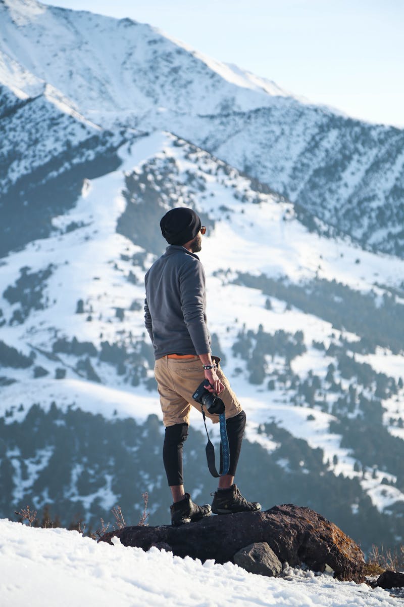 Man Wearing Gray Long-sleeved Shirt and Brown Shorts Holding Black Dslr Camera on Mountain